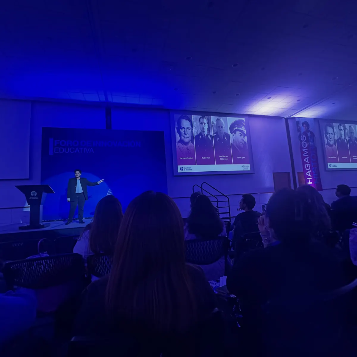 Alberto Gallegos en el escenario del Foro de Innovación Educativa, con una diapositiva de retratos proyectada y el público en primer plano